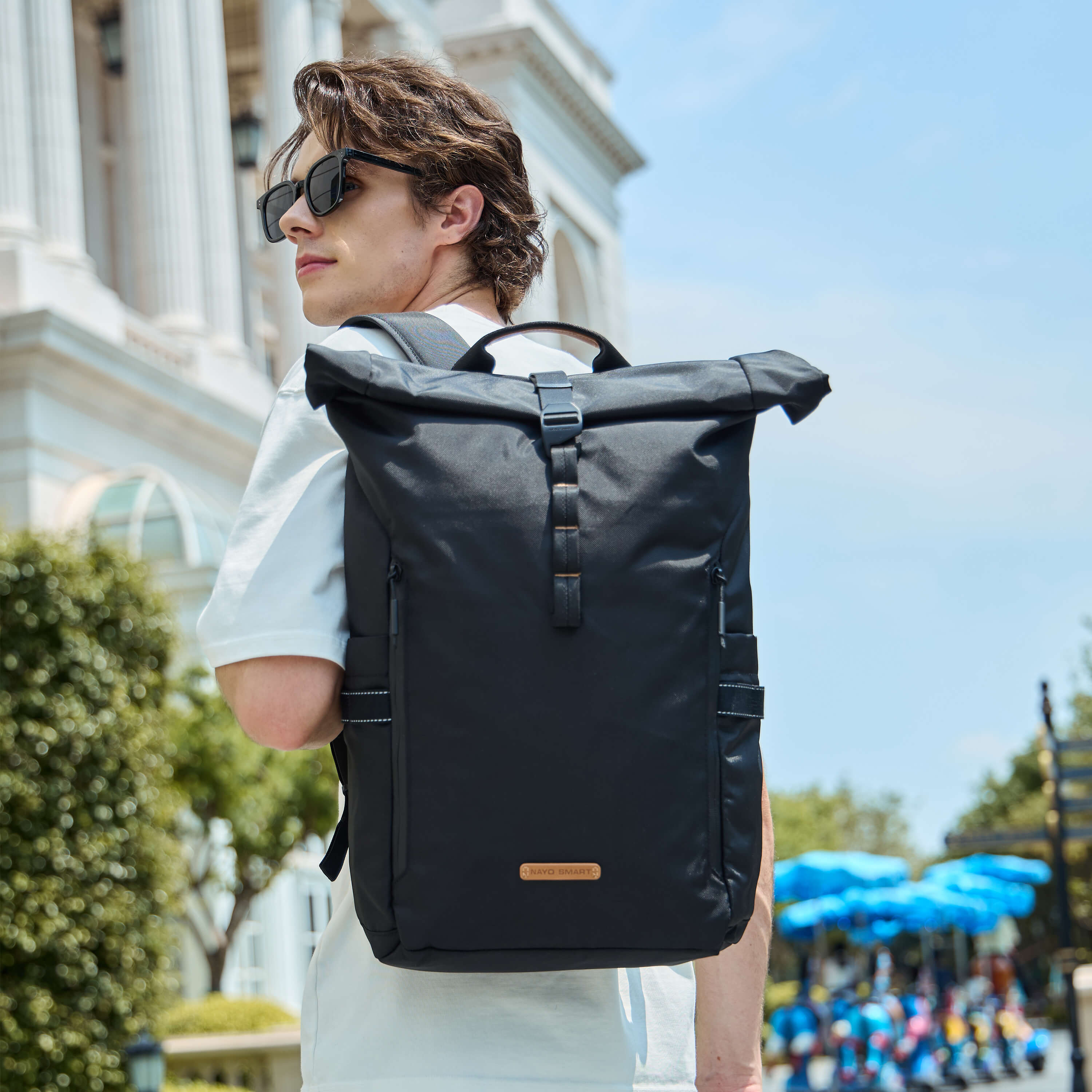 Male model wearing NayoSmart Urban U8 black roll-top backpack outdoors on city street, front view urban travel lifestyle