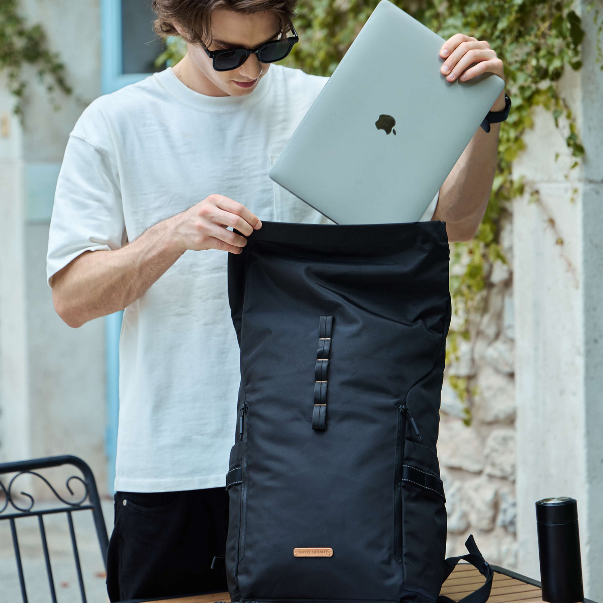 NayoSmart Urban U8 black roll‑top backpack, man placing laptop into main digital compartment outdoors, 16‑inch laptop storage for commuter travel