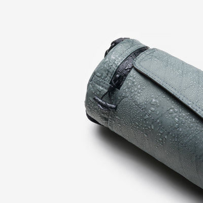 Product detail shot, Graphite Nayo Smart UL5 Cylinder Sling Bag covered with water droplets, highlighting water‑repellent X‑Pac fabric and drawstring closure