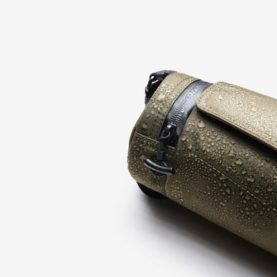 Product detail shot, Olive Nayo Smart UL5 Cylinder Sling Bag covered with water droplets, highlighting water‑repellent X‑Pac fabric and drawstring closure