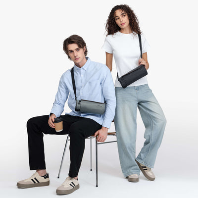 Nayo Smart Urban UL5 Cylinder Sling Bag, male and female models wearing graphite and black cylinder crossbody sling bags indoor studio shot