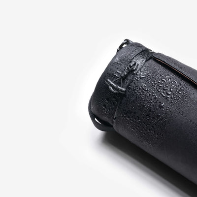 Product detail shot, black Nayo Smart UL5 Cylinder Sling Bag covered with water droplets, highlighting water‑repellent X‑Pac fabric and drawstring closure