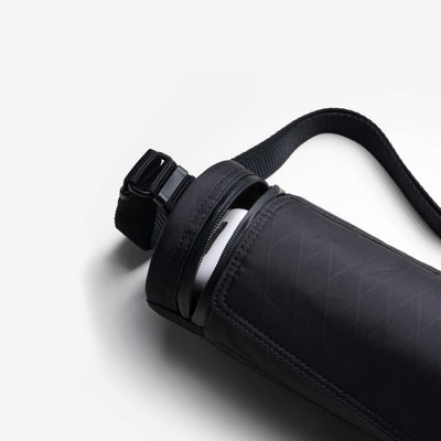 Product studio detail shot of black Nayo Smart UL5 Cylinder Sling Bag, open zipper reveals interior storage space, adjustable shoulder strap visible