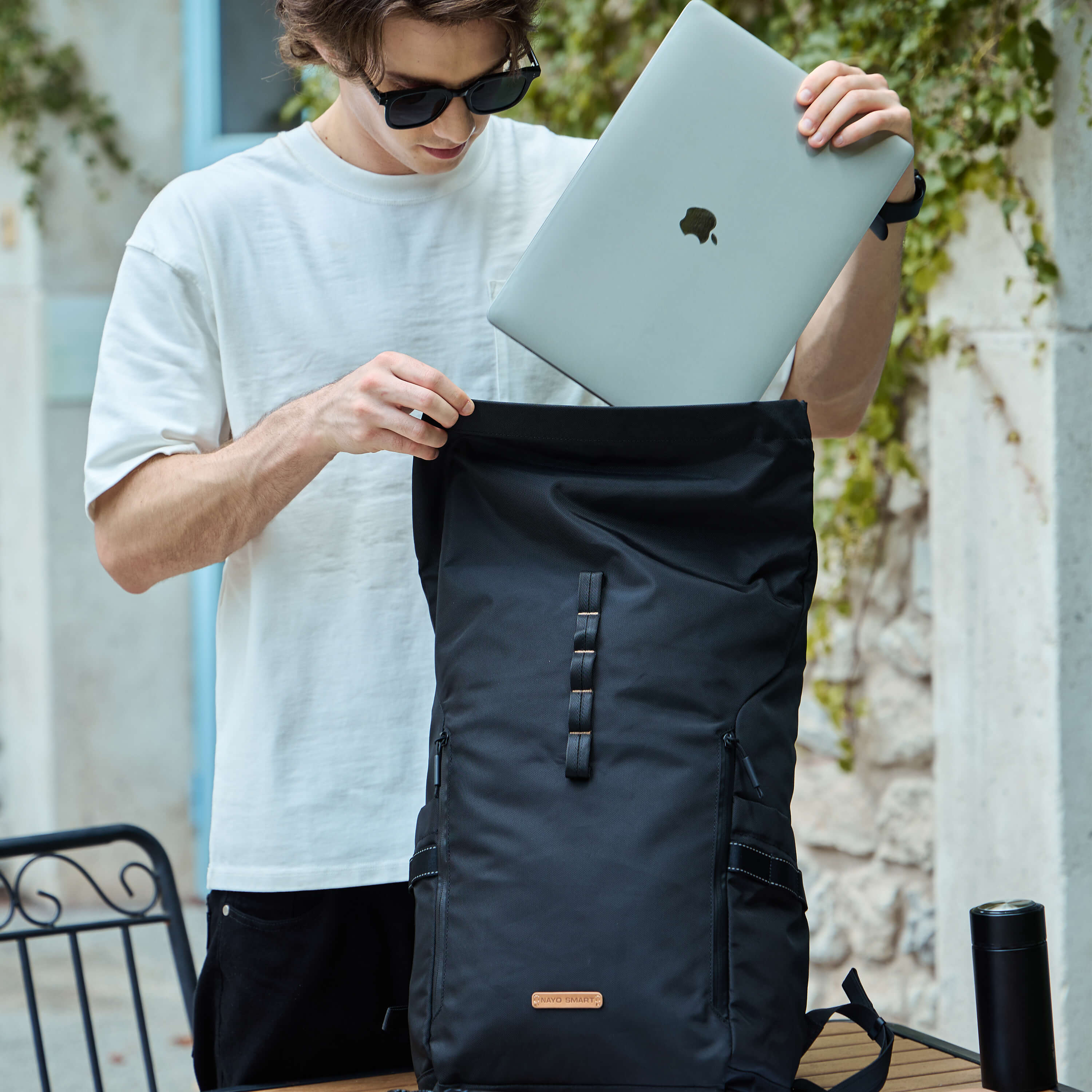 NayoSmart Urban U8 black roll‑top backpack, man placing laptop into main digital compartment outdoors, 16‑inch laptop storage for commuter travel